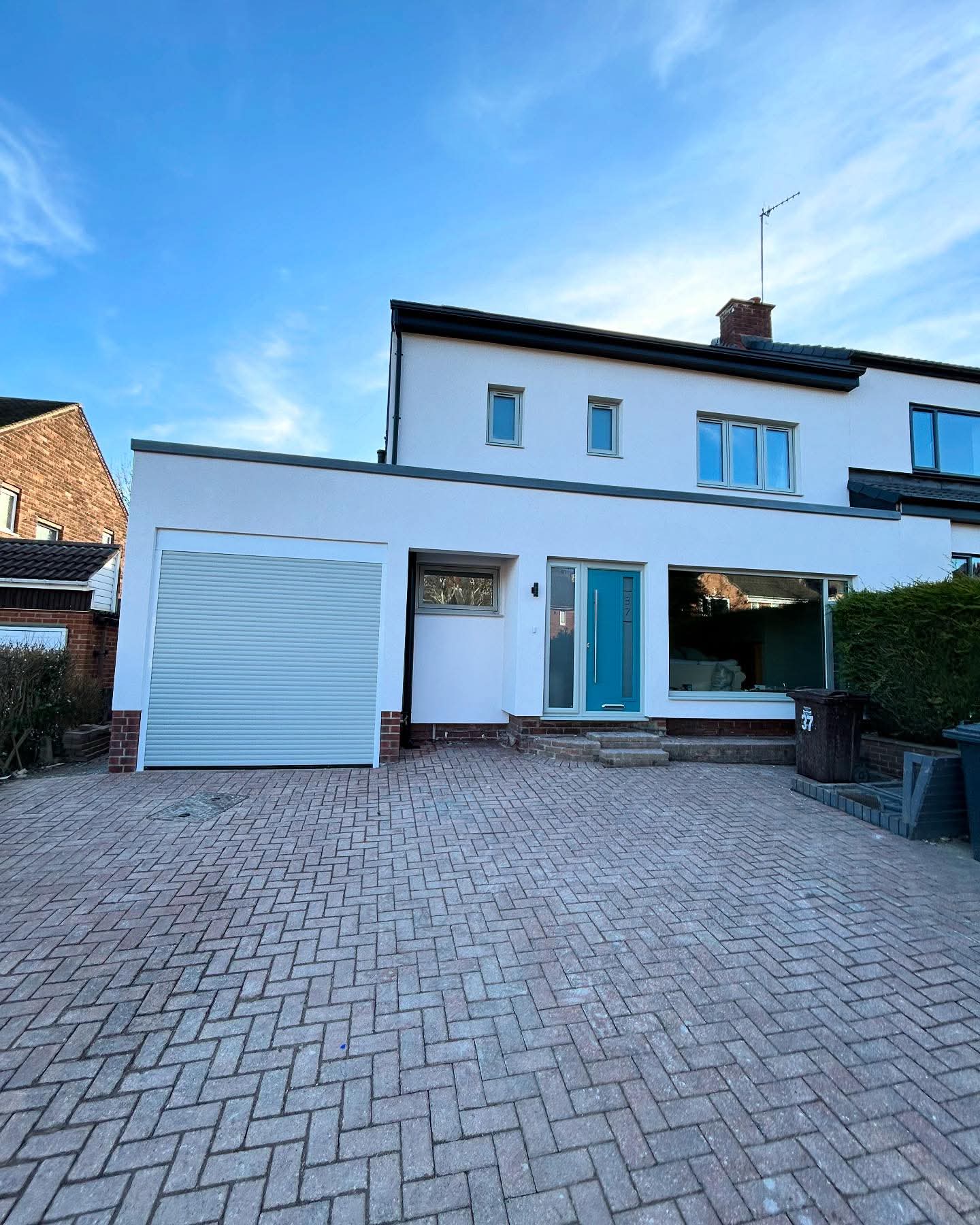 Front of a home finished in crisp white render with a teal front door